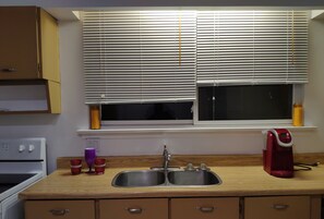 A kitchen with a sink, a stove, and a window with blinds.