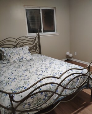 A bed with a floral bedspread, a window with blinds, and a wall-mounted light fixture.