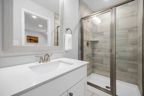 A modern bathroom with a white sink, a large mirror, and a glass-enclosed shower.