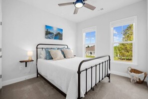 A bedroom with a bed, a ceiling fan, a window with a view, and a wall-mounted lamp.