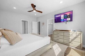 A bedroom with a bed, dresser, ceiling fan, and a TV displaying streaming services.