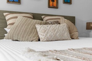 Uma cama com várias almofadas e um cobertor, cabeceira de madeira e quadros na parede.