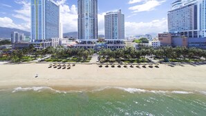 Un hotel frente a la playa con varios edificios altos, una playa de arena y palmeras.