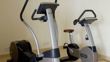 Two stationary exercise bikes in a room with a plain wall and a tiled floor.
