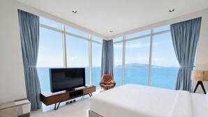 Un dormitorio con una cama grande, televisión, una silla y vista al mar.