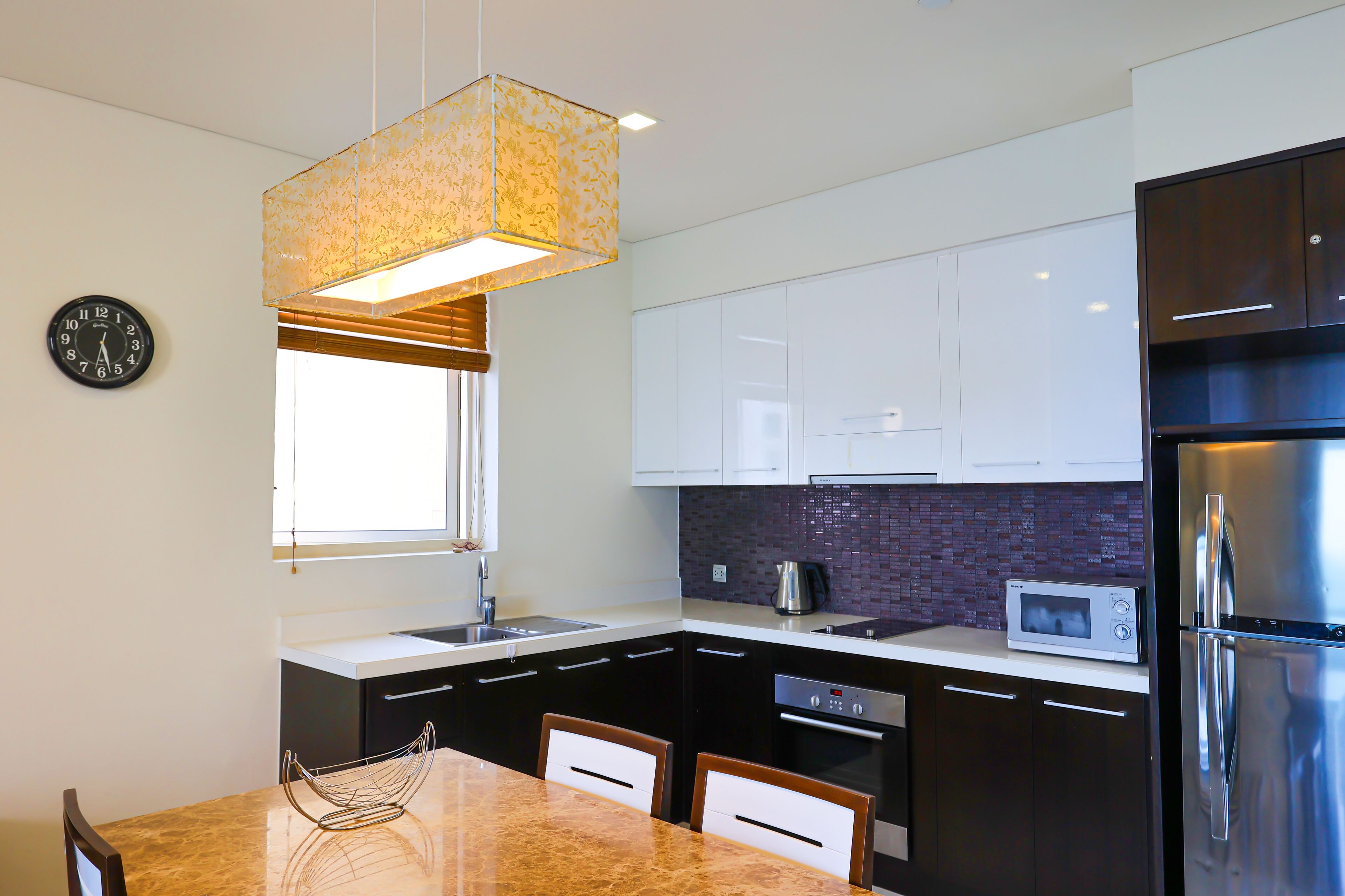A modern kitchen with black cabinets, a stainless steel refrigerator, a microwave, and a dining area with a marble table and chairs.
