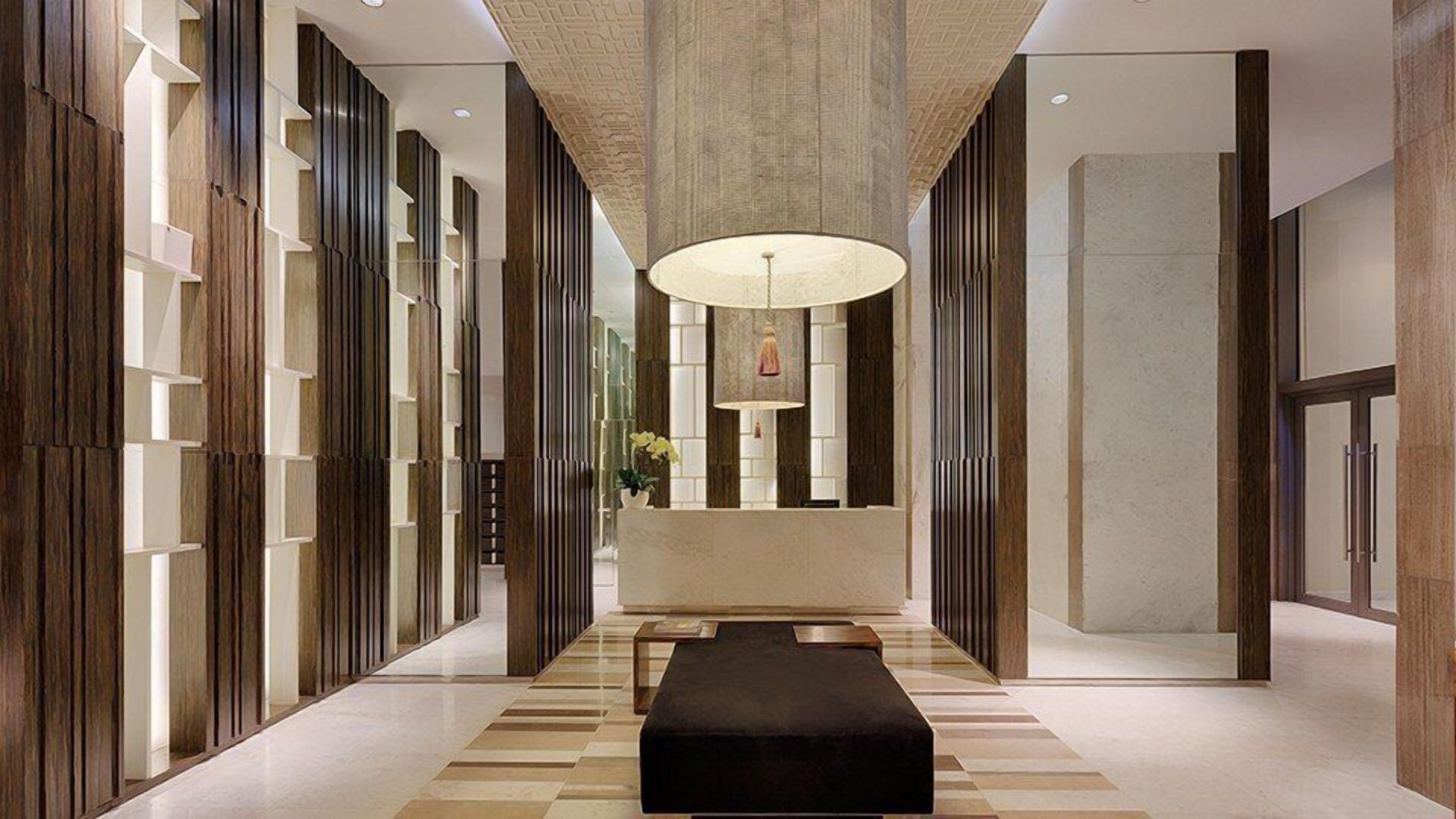 A modern hallway with a central bench, patterned flooring, and a large pendant light.