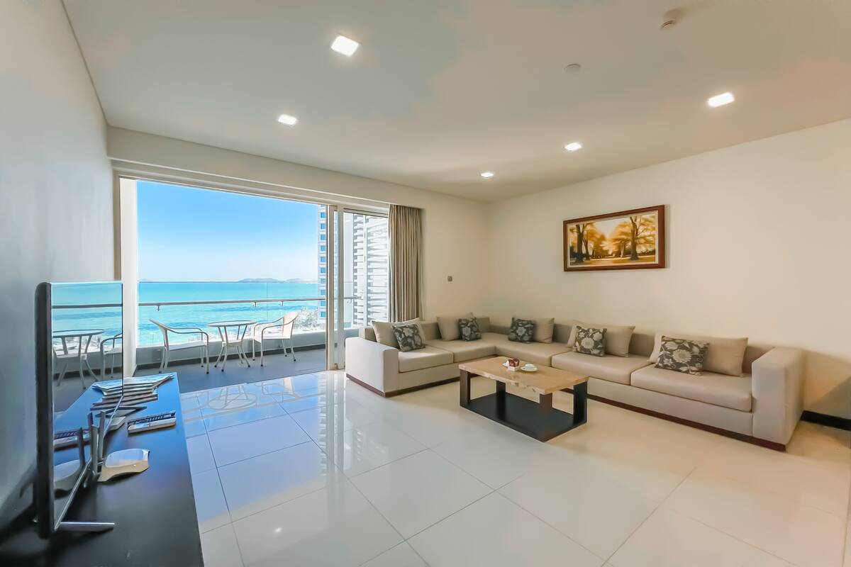 A modern living room with a sofa set, a coffee table, and a large window offering a view of the sea.