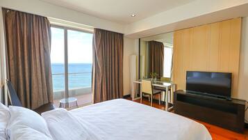 Una habitación de hotel con una cama grande, un escritorio, un televisor y vista al mar.