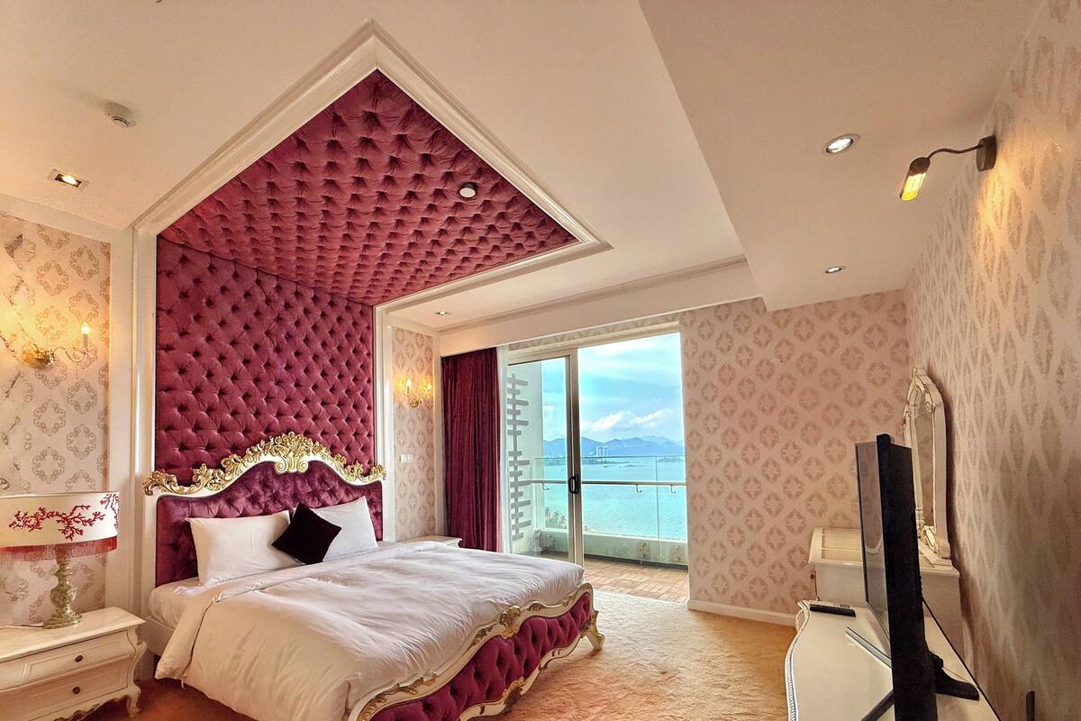 A spacious bedroom with a large bed, a balcony with a view, and a television on a dresser.