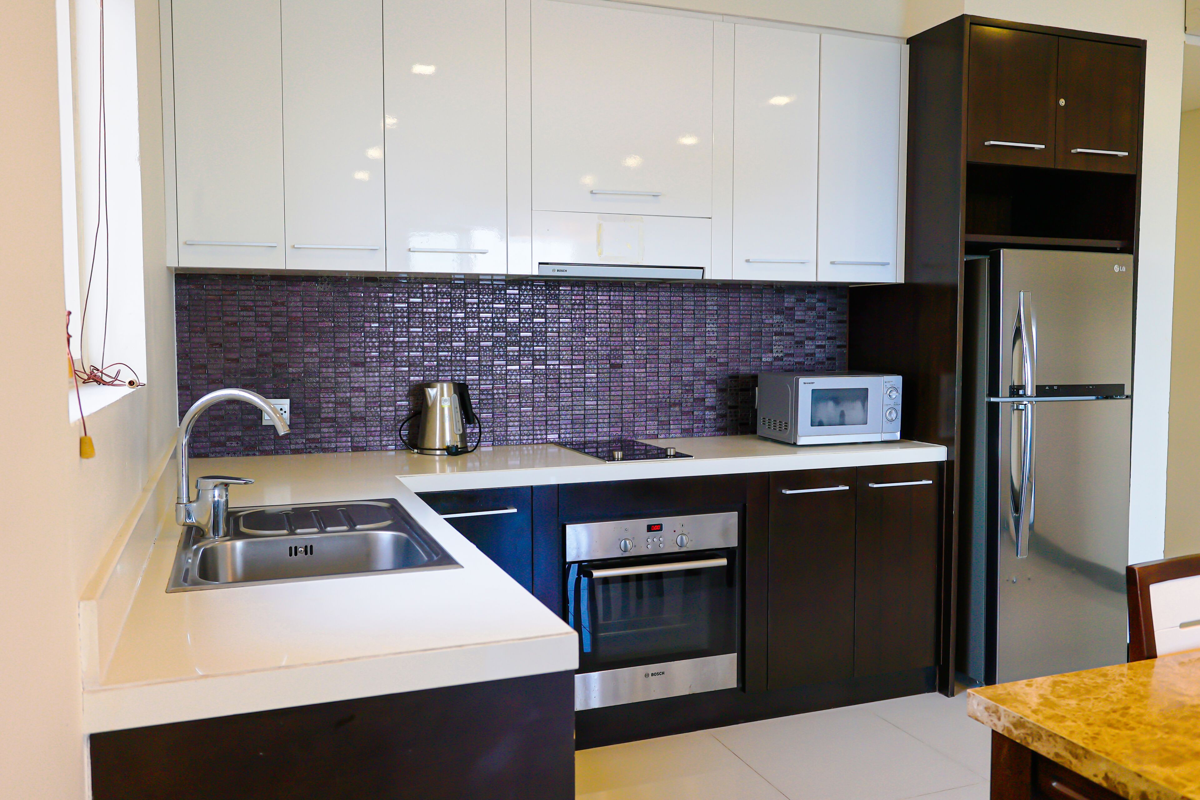 A modern kitchen with white cabinets, a stainless steel refrigerator, a microwave, and an oven.