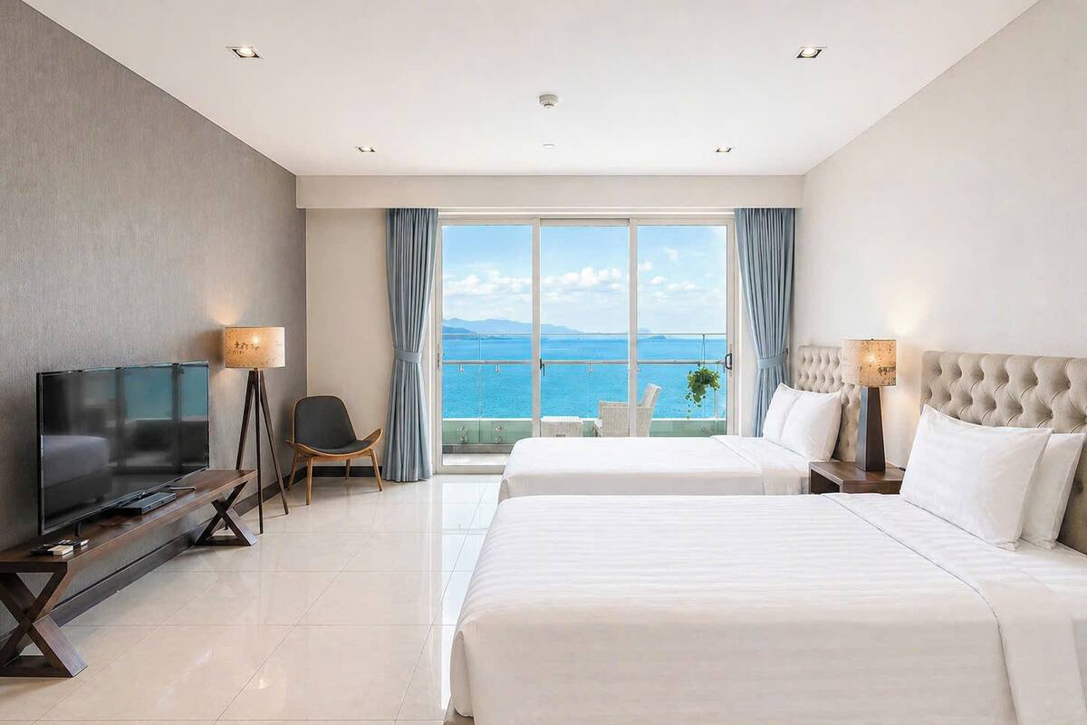 A hotel room with two beds, a TV, a chair, and a balcony with a view of the sea.