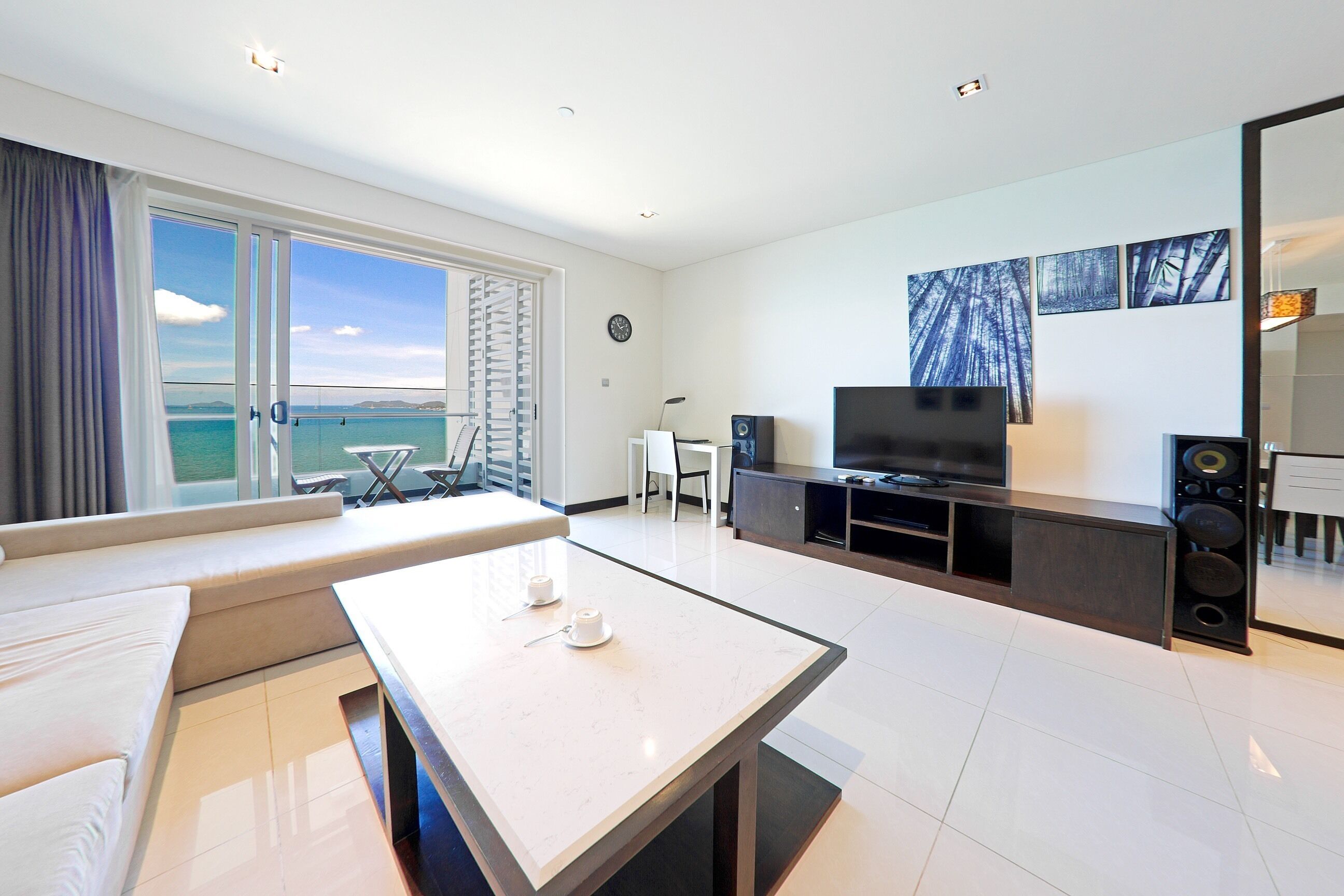 A modern living room with a large window, a sofa, a coffee table, a TV, and a speaker system.