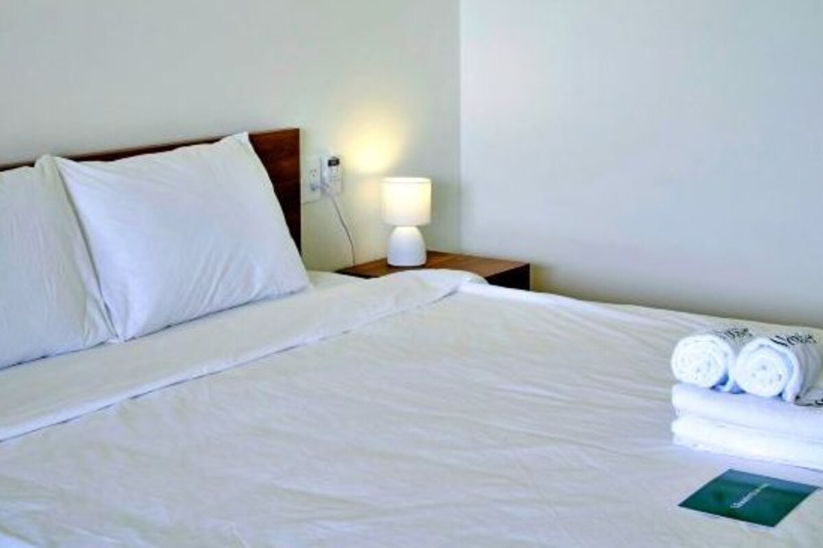 Un lit bien fait, avec du linge de lit blanc, une lampe de chevet et des serviettes pliées sur la table de chevet.