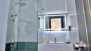 Een moderne badkamer met een douchecabine van glas, een wastafel met spiegel en toiletartikelen.