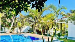 A swimming pool surrounded by palm trees and a building with a tiled roof. - The White House Villa (Ahangama)