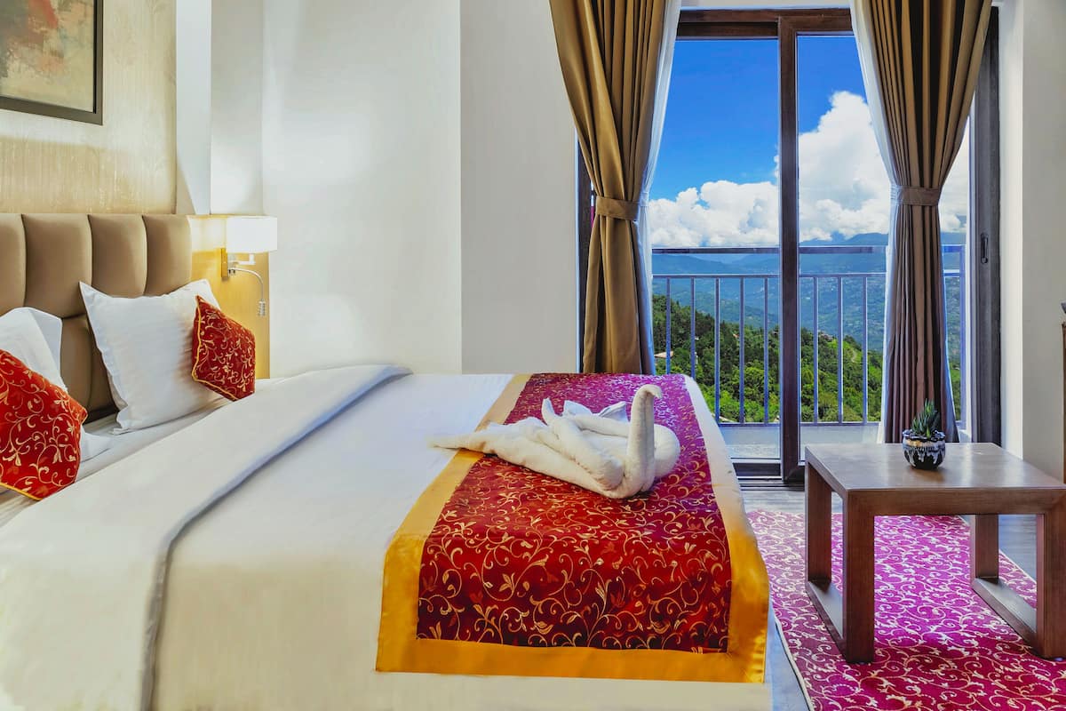 Une chambre d’hôtel avec un grand lit, une vue sur les montagnes et un balcon avec des rideaux.
