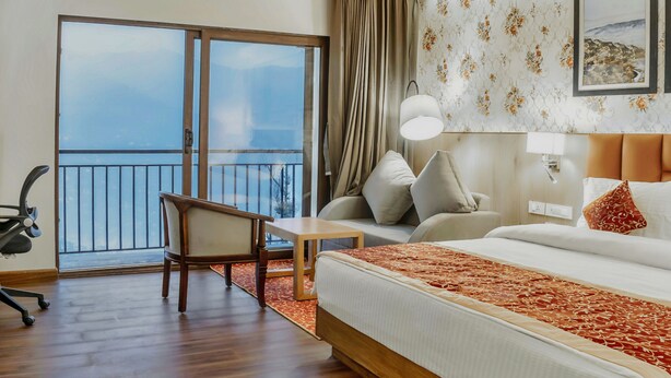 A hotel room with a large bed, a desk, a chair, a balcony with a view, and a wall with a floral pattern. - The Aryan Hotel Gangtok (Gangtok)