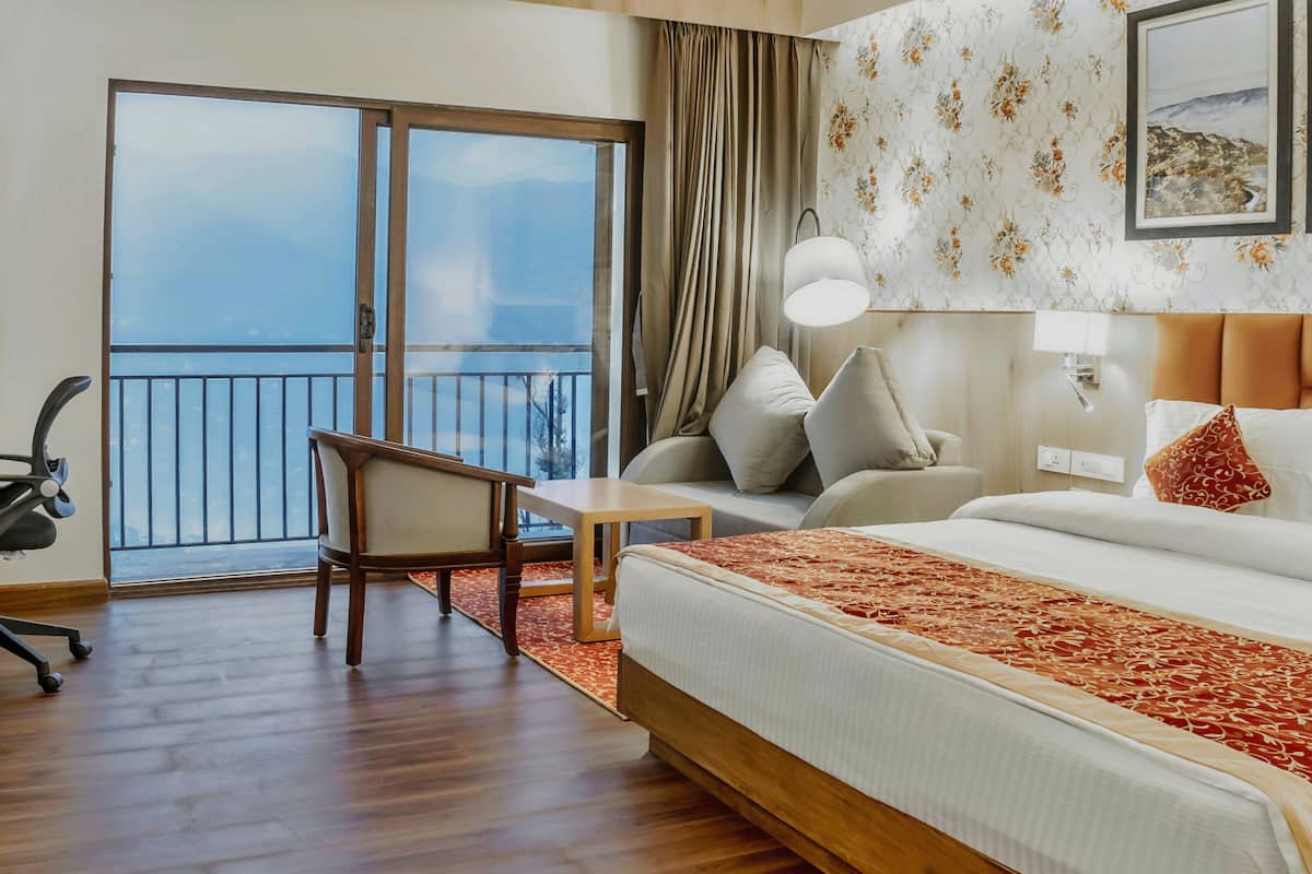 Une chambre d’hôtel avec un grand lit, un bureau, une chaise, un balcon avec vue et un mur orné d’un motif floral.