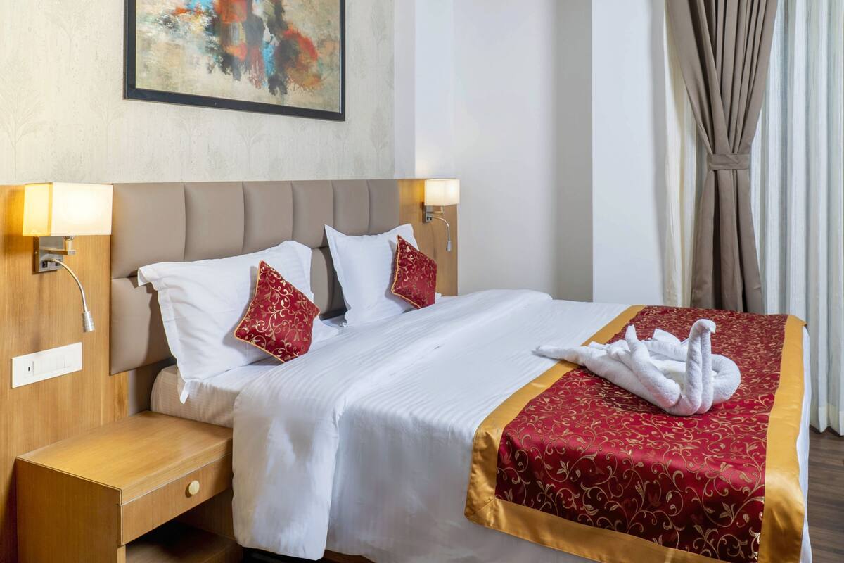 Une chambre d’hôtel avec un lit, deux lampes de chevet, une table de chevet et une couvre-lit rouge et or.