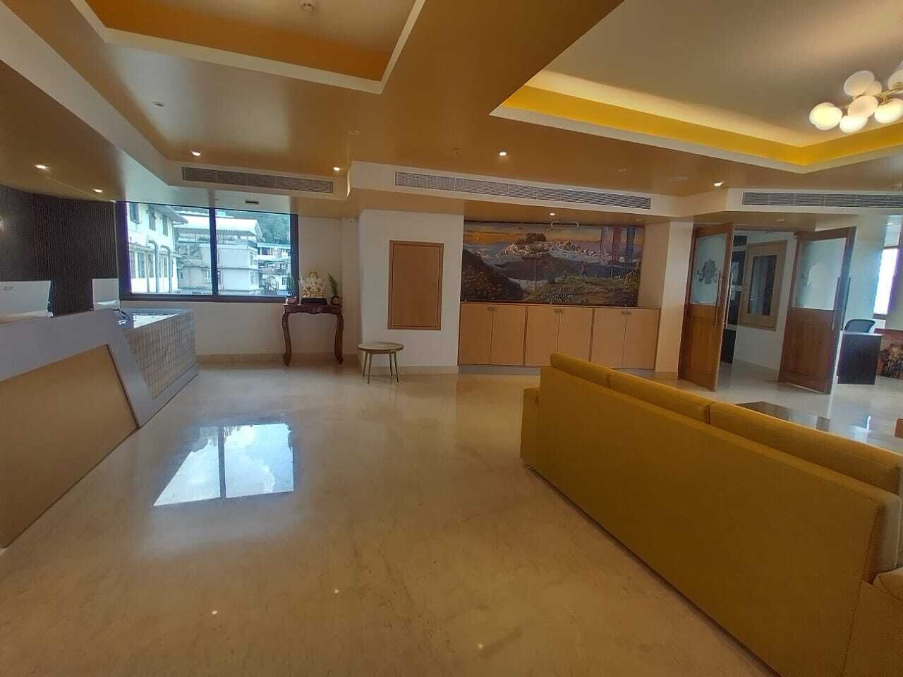 Un vestíbulo amplio con mostrador de recepción, un sofá amarillo y un ventanal con vistas al exterior.