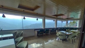 A spacious dining area with high ceilings and large windows offering a view of the mountains. - The Aryan Hotel Gangtok (Gangtok)