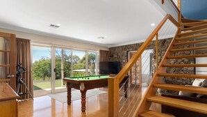 Amplia habitación con mesa de billar, escalera de madera y pared de piedra.