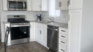 A modern kitchen with white cabinets, stainless steel appliances, and a wooden floor.