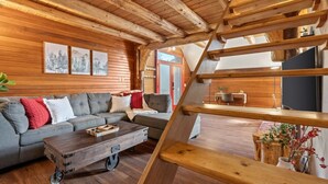 A cozy living room with a wooden ceiling, a sofa, a coffee table, and a staircase.