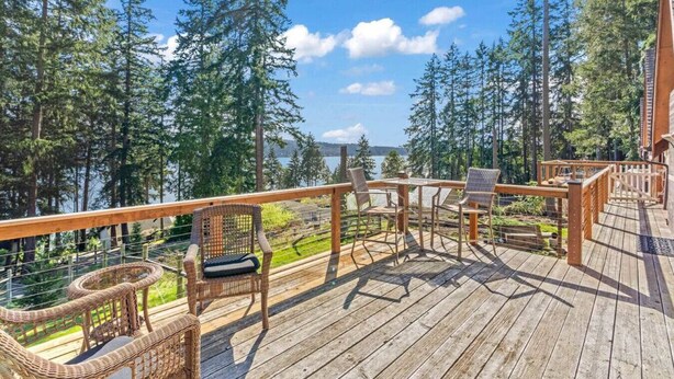 A wooden deck with wicker furniture overlooking a forest and a lake.
