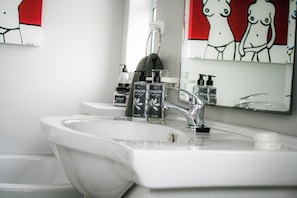 A bathroom with a white sink, two faucets, and two hand soap dispensers.