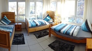 A cozy bedroom with two wooden beds, a small wooden nightstand, and a large window providing a view of the outside. - 80sqm two-room apartment - Wipfelder Montuerzimmer (Wipfeld)