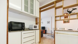 Eine Küche mit weißen Schränken, einer Mikrowelle und einer Kaffeemaschine. Ein Holzregal zeigt Dekorationen und ein gerahmtes Bild hängt an der Wand.