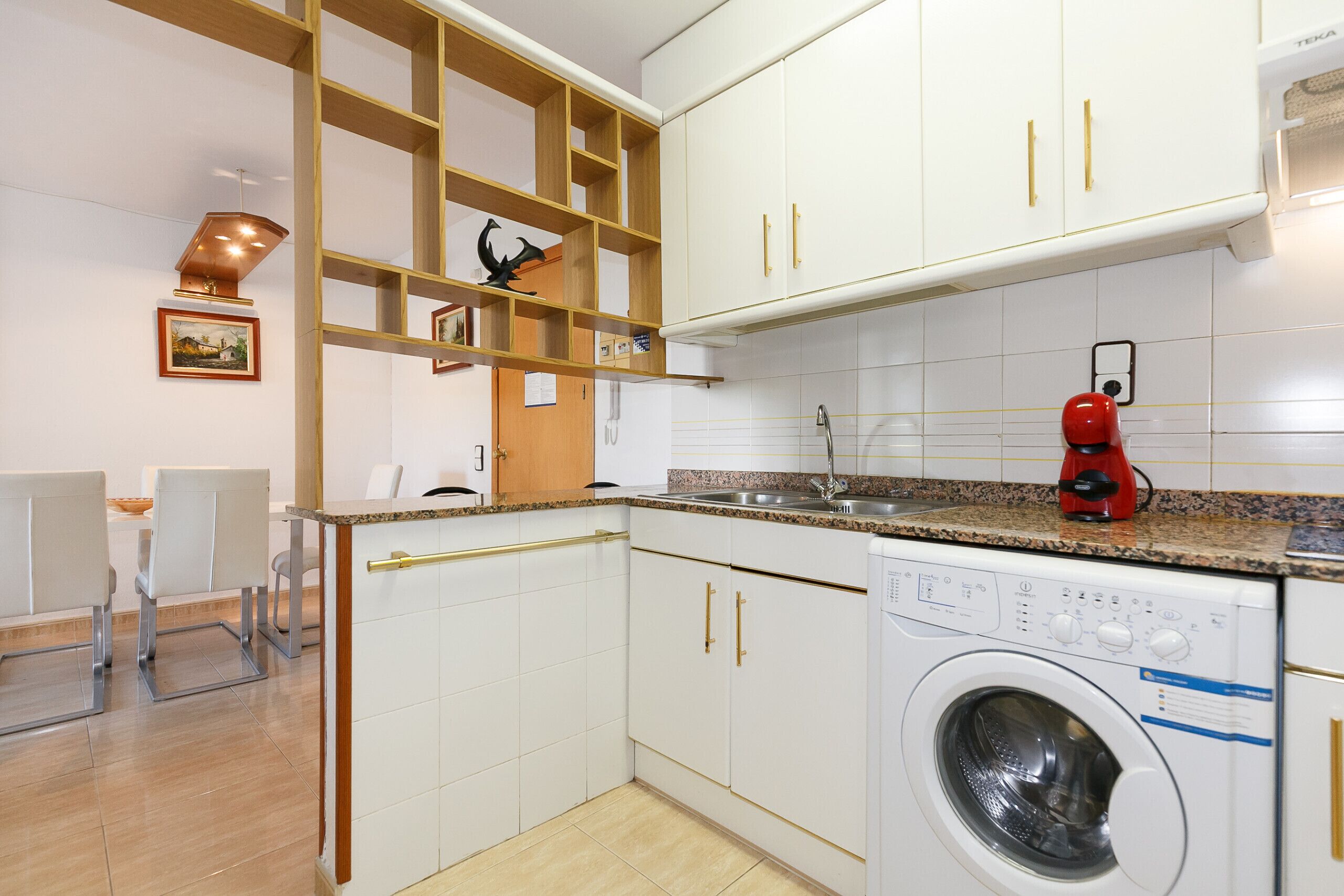Une cuisine compacte avec des meubles blancs, un lave-linge encastré et un plan de travail en granit.