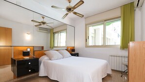 Ein Schlafzimmer mit Bett, Nachttischen, einem Spiegel, einem Deckenventilator und einem Fenster mit Vorhängen.