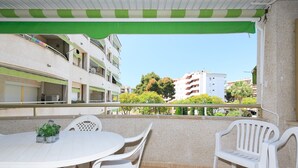 Ein Balkon mit weißem Tisch und Stühlen, einer grünen Markise und Blick auf Gebäude und Bäume.