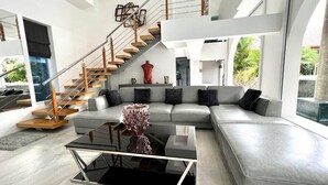 A modern living room with a grey sectional sofa, a glass coffee table, and a wooden staircase.