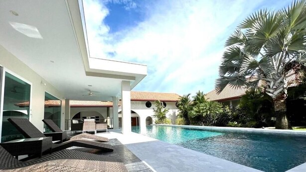 A modern pool area with lounge chairs, a clear pool, and surrounding palm trees.