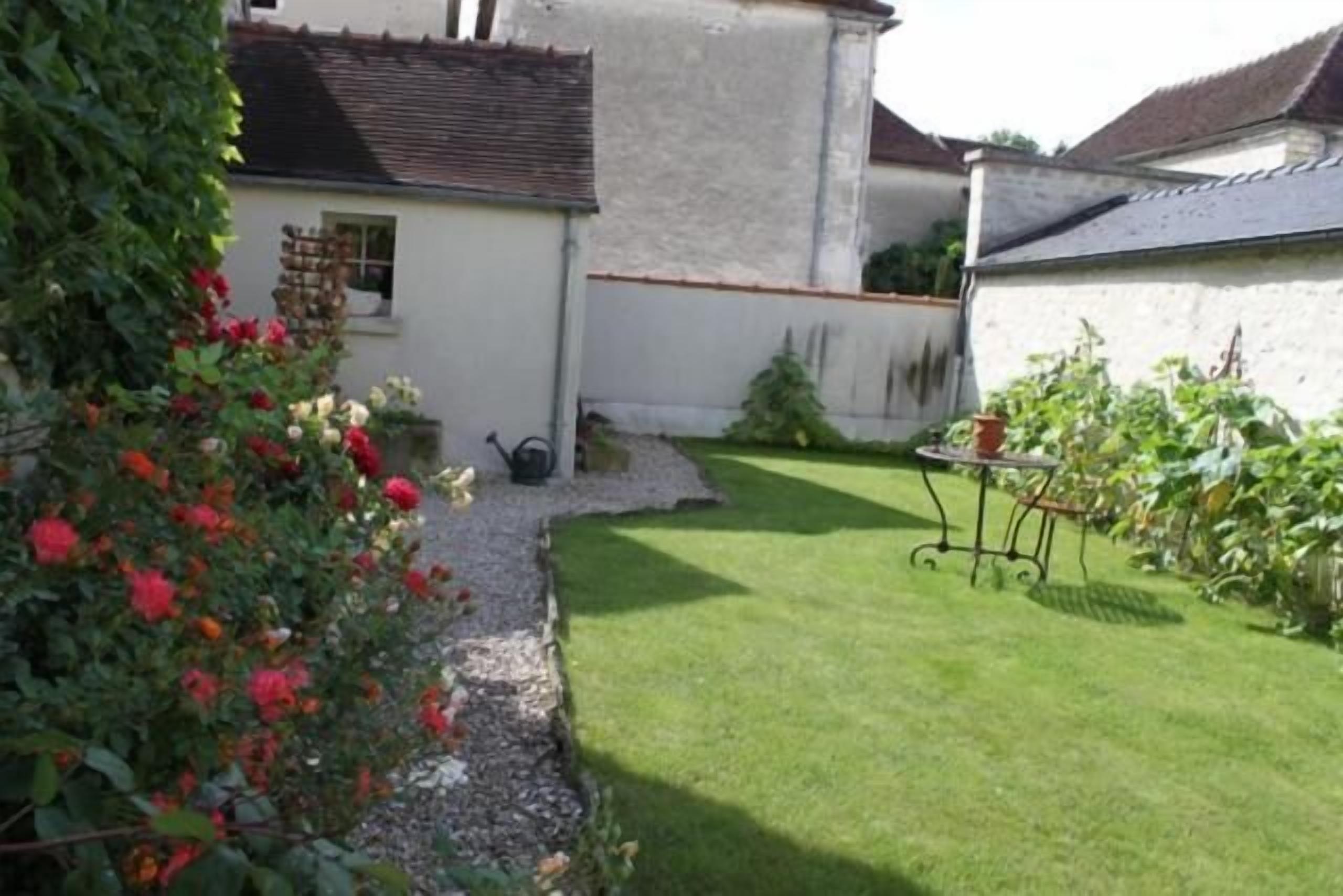A garden with a white building, a small window, and a table with chairs.