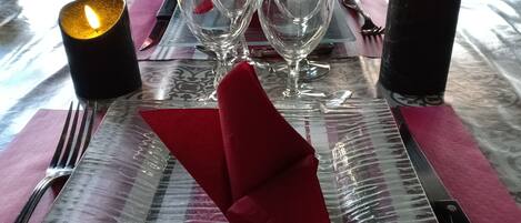A table set with clear glassware, a folded red napkin, and two lit candles.
