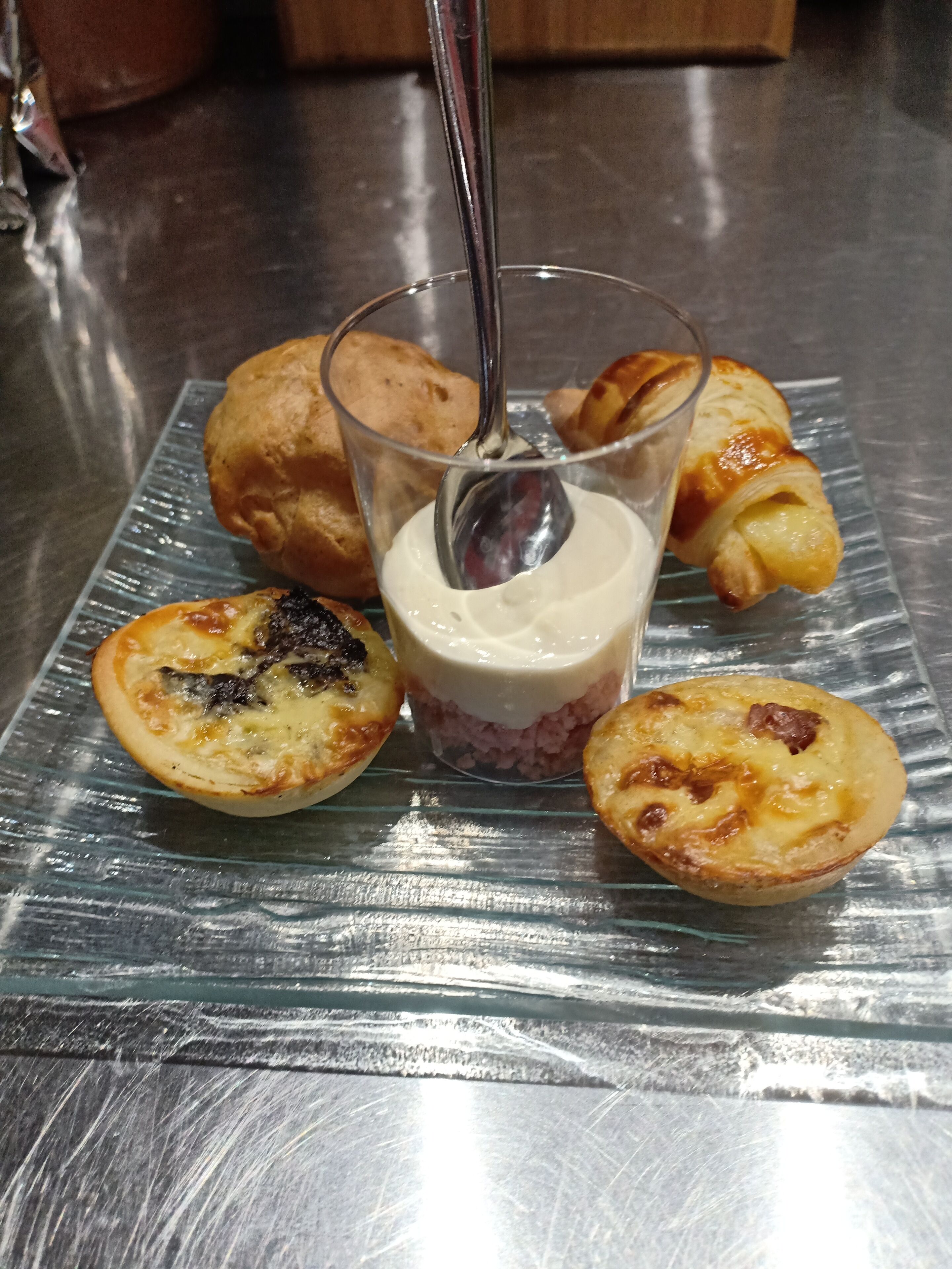A glass plate with pastries and a dessert on a reflective surface.