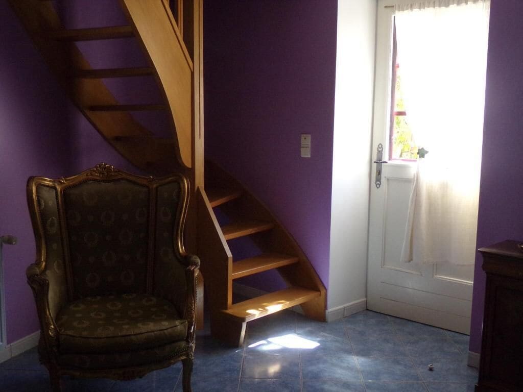 Una habitación con pared morada, escalera de madera, una silla y una puerta con ventana.