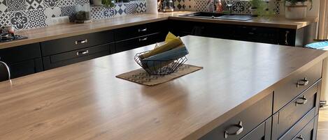 Una cocina moderna con una isla grande, sillas negras y una variedad de plantas y utensilios de cocina.