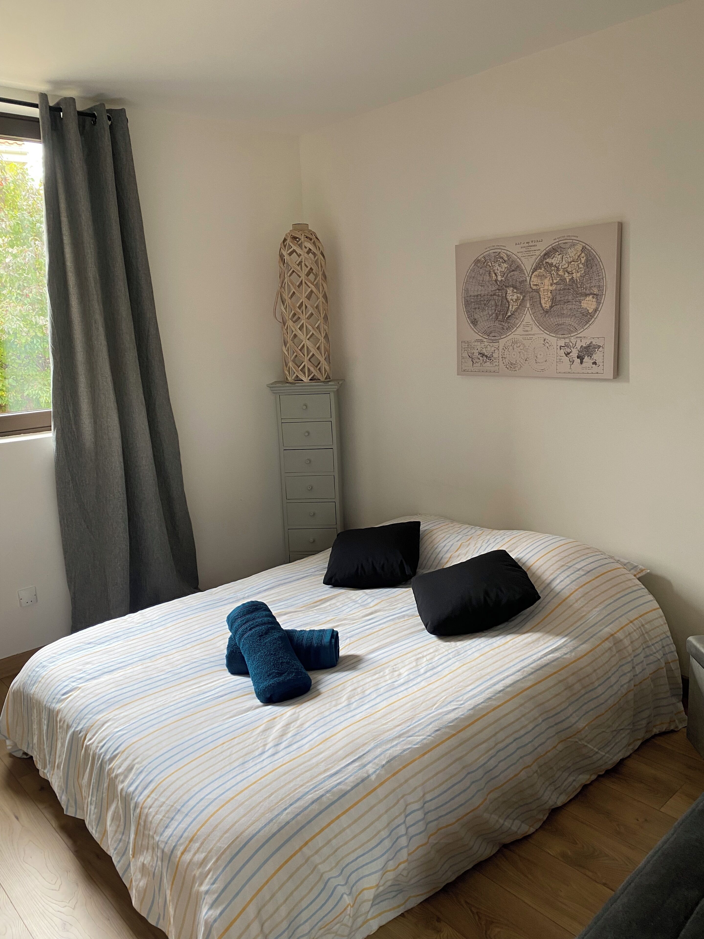 Un dormitori amb un llit, un aparador, una obra d'art amb un globus i una finestra amb cortines.