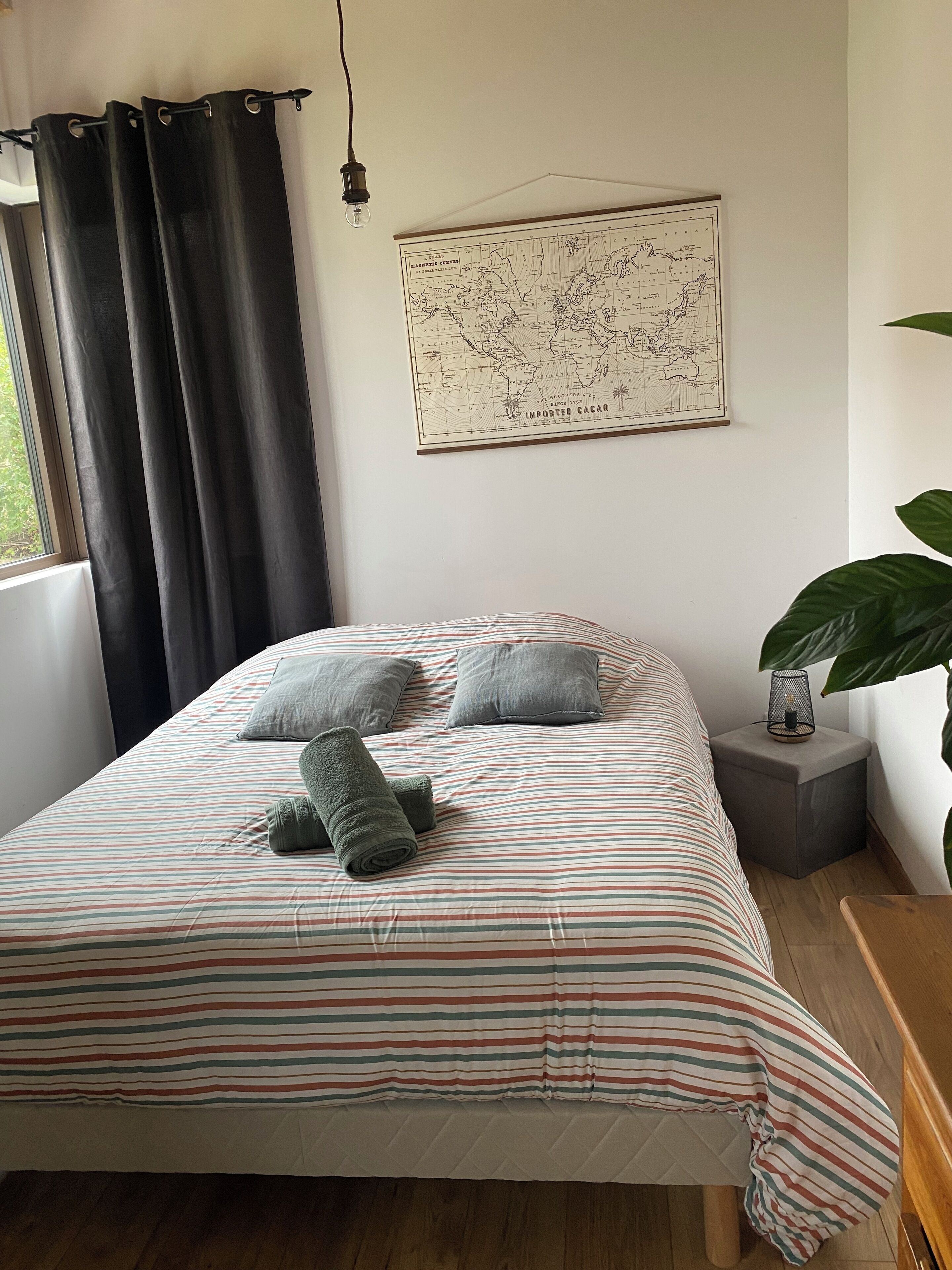 A neatly made bed with striped bedding, a map on the wall, and a small bedside table with a lamp.