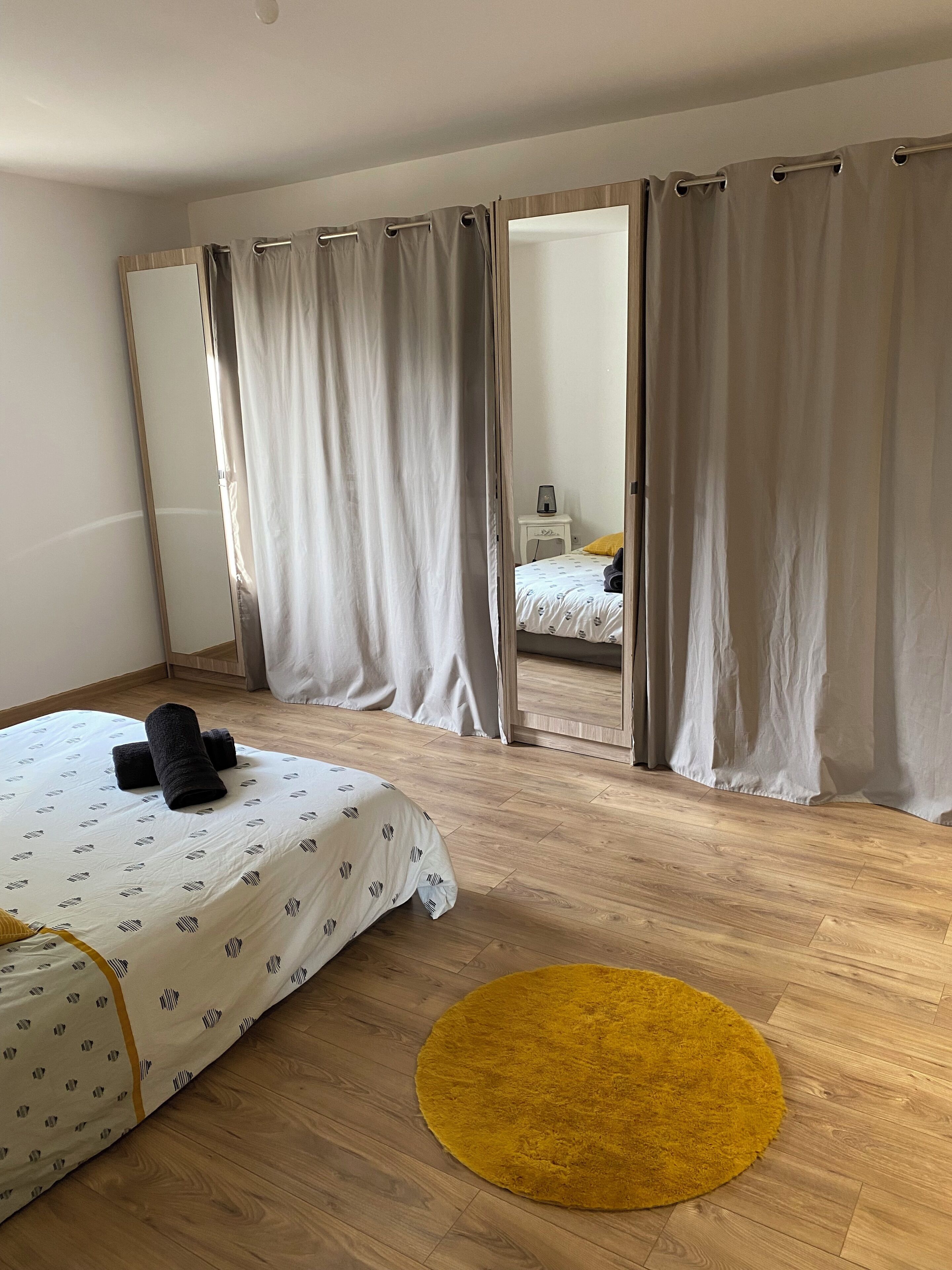 Une chambre à coucher avec un lit, un tapis jaune et un miroir agrémenté de rideaux.
