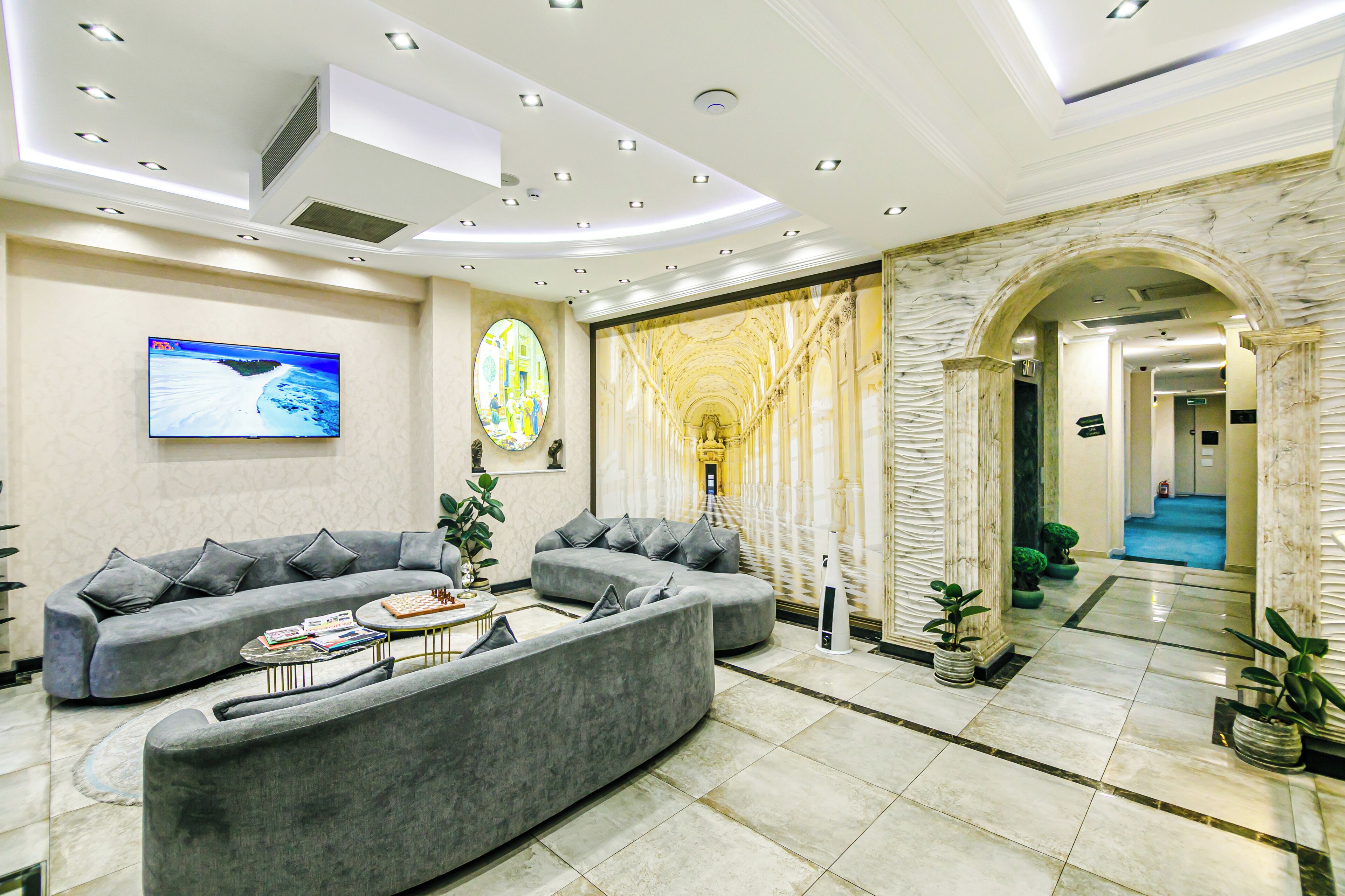 A modern living room with grey sofas, a flat-screen TV, and a marble wall.