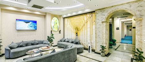 A modern living room with grey sofas, a flat-screen TV, and a marble wall.