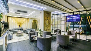 A modern lounge area with sofas, armchairs, and a coffee table. A television is mounted on a glass wall, and there is a staircase leading to an outdoor area. - Essam Deluxe Hotel (Baku)