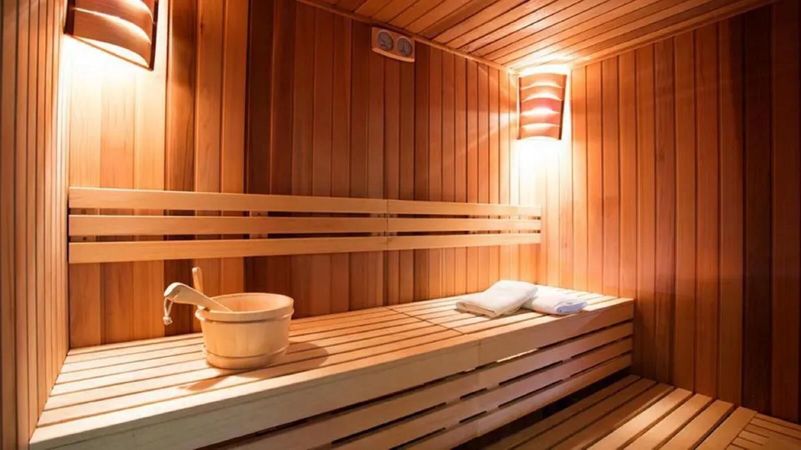 A sauna with wooden benches, a wooden bucket, and a wall-mounted light fixture.